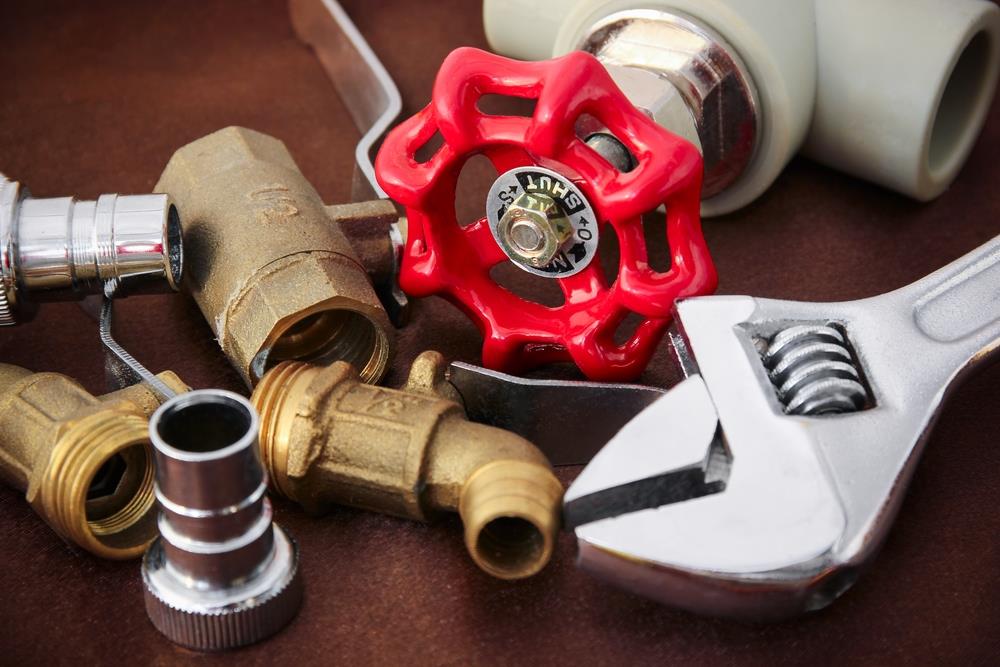 A collection of plumbing tools and fittings, including a red valve handle, metal wrench, and various brass and plastic pipe components, on a brown surface — perfect for an emergency plumber in Atlanta.