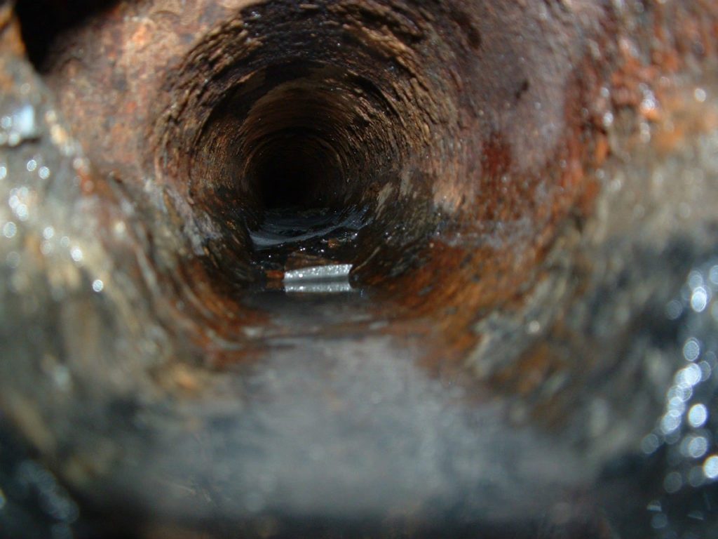 Close-up image of the interior of a rusty and corroded pipe with liquid visible at the bottom, ideal for a plumbing inspection.