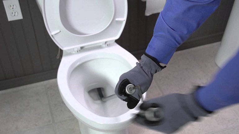 An emergency plumber in Atlanta wearing gloves cleans a toilet meticulously with a brush and cleaning solution.