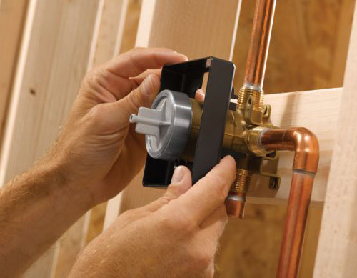 A person is installing a plumbing fixture with copper pipes and a plastic component within a wooden framework, possibly needing an emergency plumber in Atlanta.