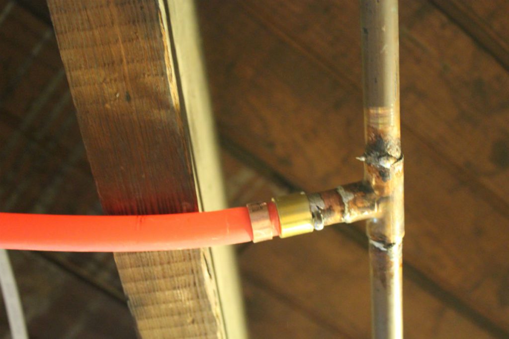 A red plastic pipe is connected to a metal pipe via a brass fitting, often inspected during regular plumbing inspections.