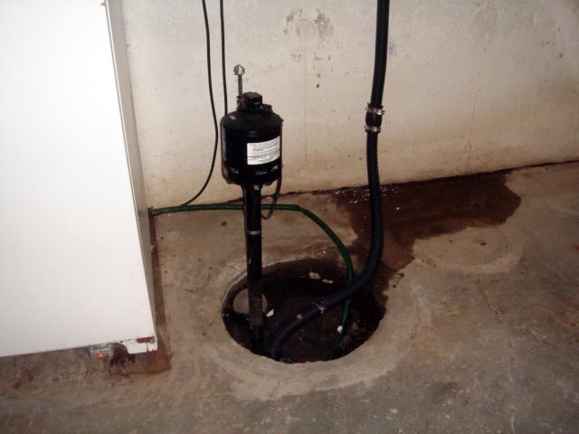 A sump pump is installed in a concrete floor, with hoses and electrical wires connected, in a basement setting. For emergencies like burst pipe repair or regular maintenance such as drain cleaning services, rely on professional 24/7 plumbing service to ensure everything runs smoothly.