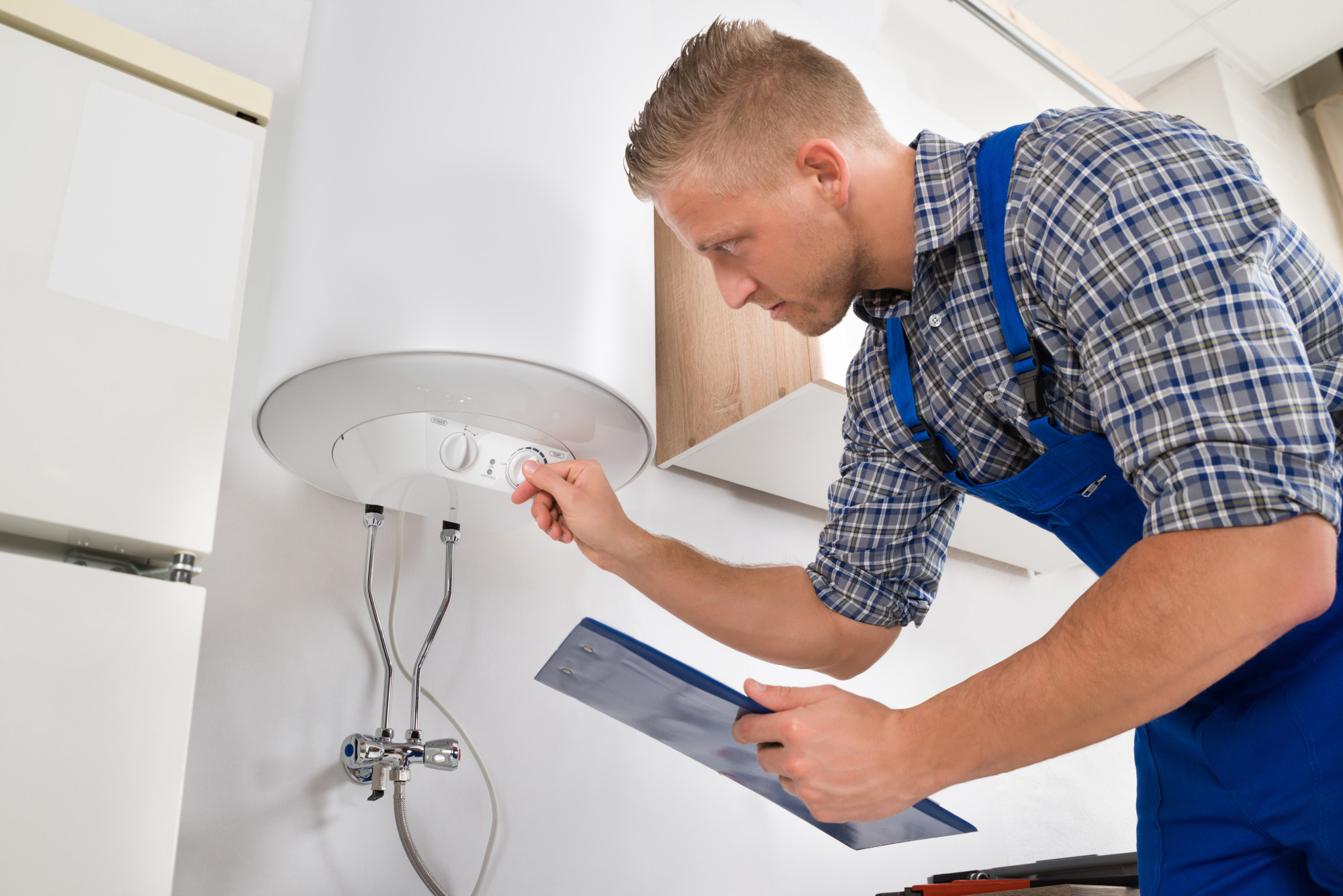 A technician in a blue overall adjusts the settings on a water heater while holding a clipboard, showcasing expertise in water heater repair.